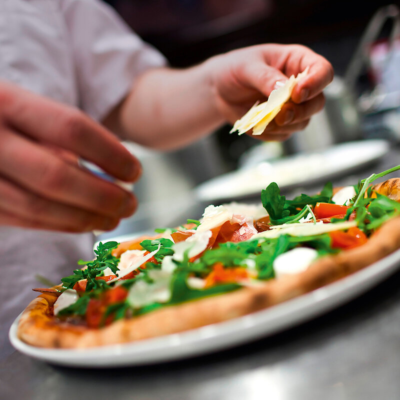Eine Pizza mit Tomaten und Rucola wird mit Parmesan bestreut.