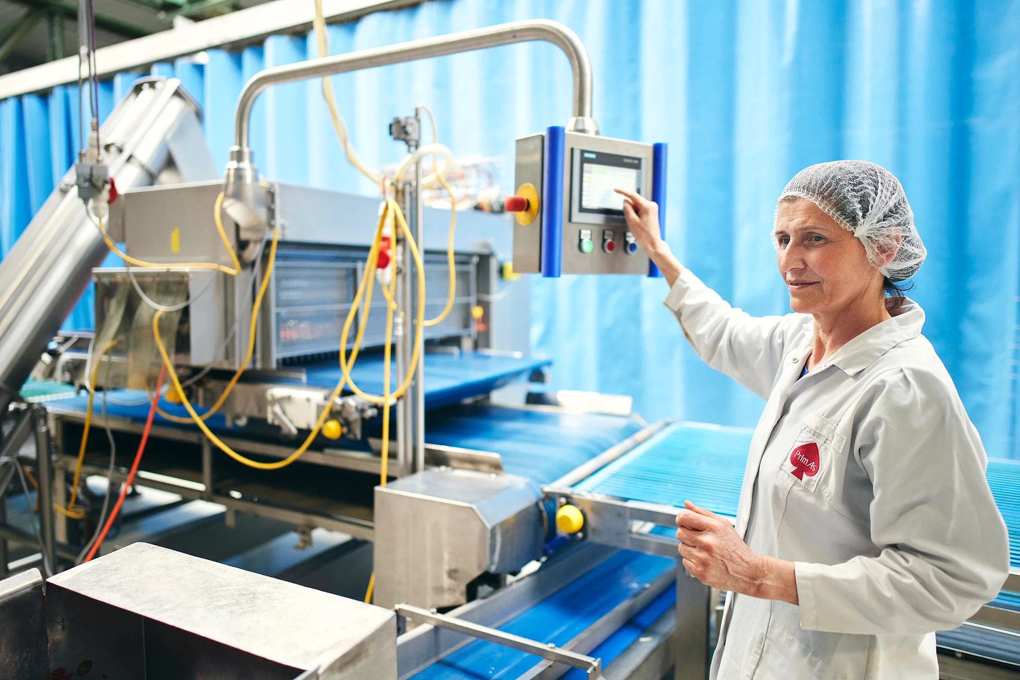 Eine Mitarbeiterin steht in Arbeitskleidung an einer Produktionsmaschine und tippt auf dem Display.