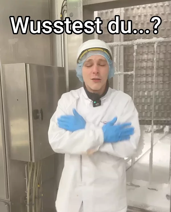 Mitarbeiter steht in Arbeitskleidung mit verschränkten Armen in der Produktion.