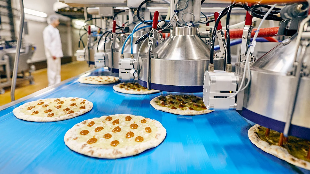 Mitarbeiter in Arbeitskleidung neben Produktionsmaschine.