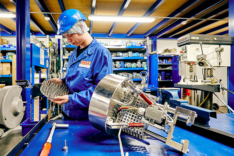 Mitarbeiter in Arbeitskleidung schraubend an einer Maschine.