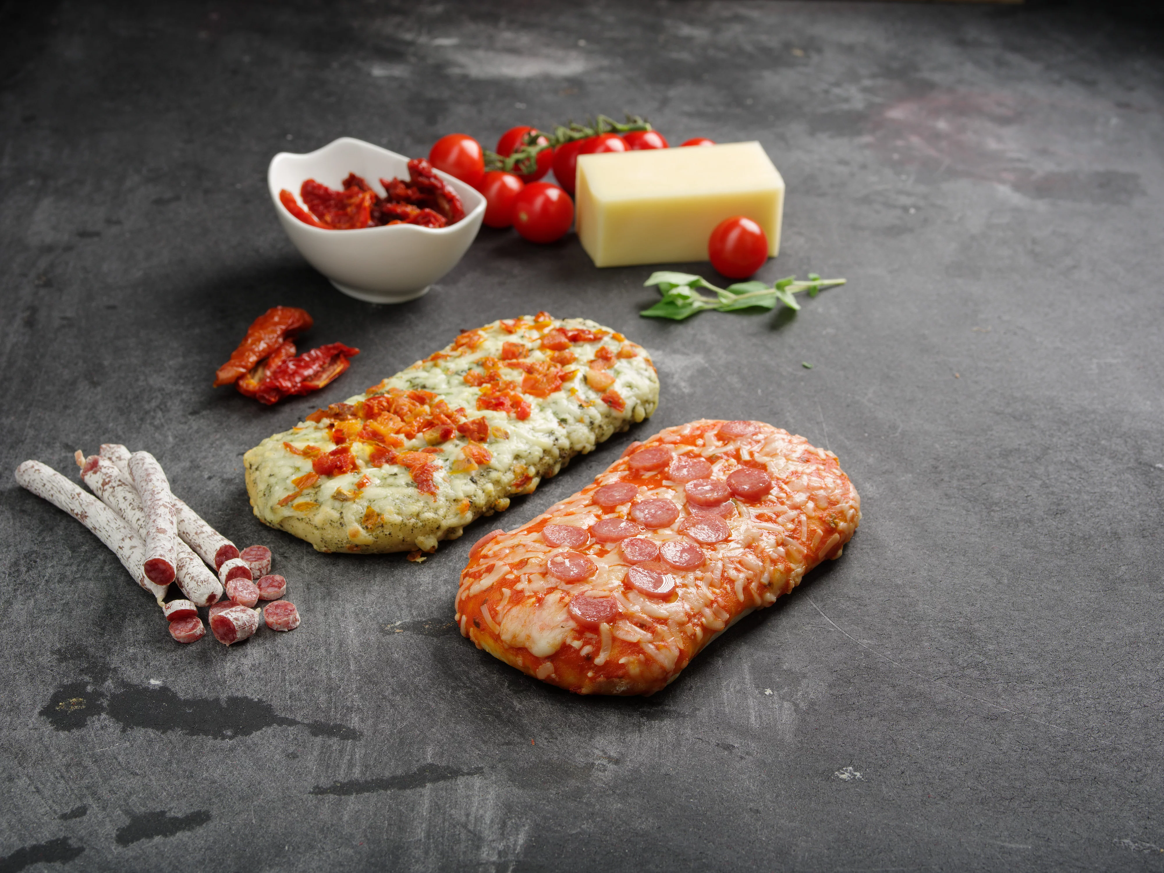 Zwei Pizzabrote dekoriert mit Salami, Tomaten, Käse, Basilikum und Chillis.