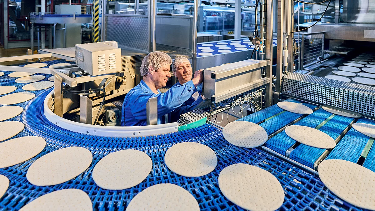 Zwei Mitarbeitende in Arbeitskleidung in der Pizza-Produktion am Band.