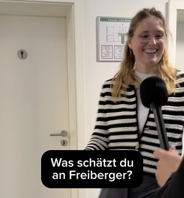 Eine Frau läuft in Arbeitskleidung über den Flur, bekommt ein Mikrofon hingehalten.