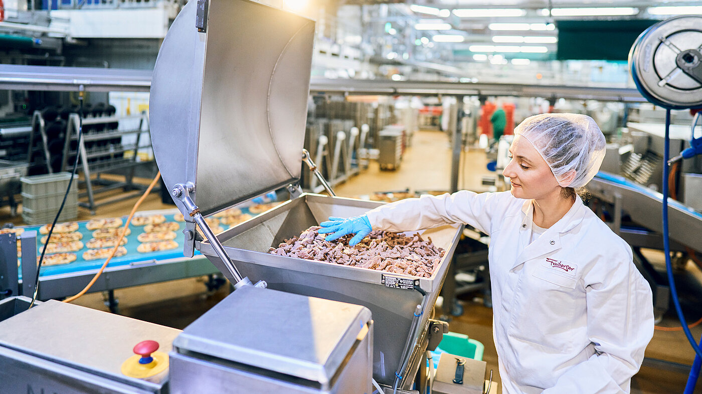 Mitarbeiterin in Arbeitskleidung vor Produktionsmaschine.