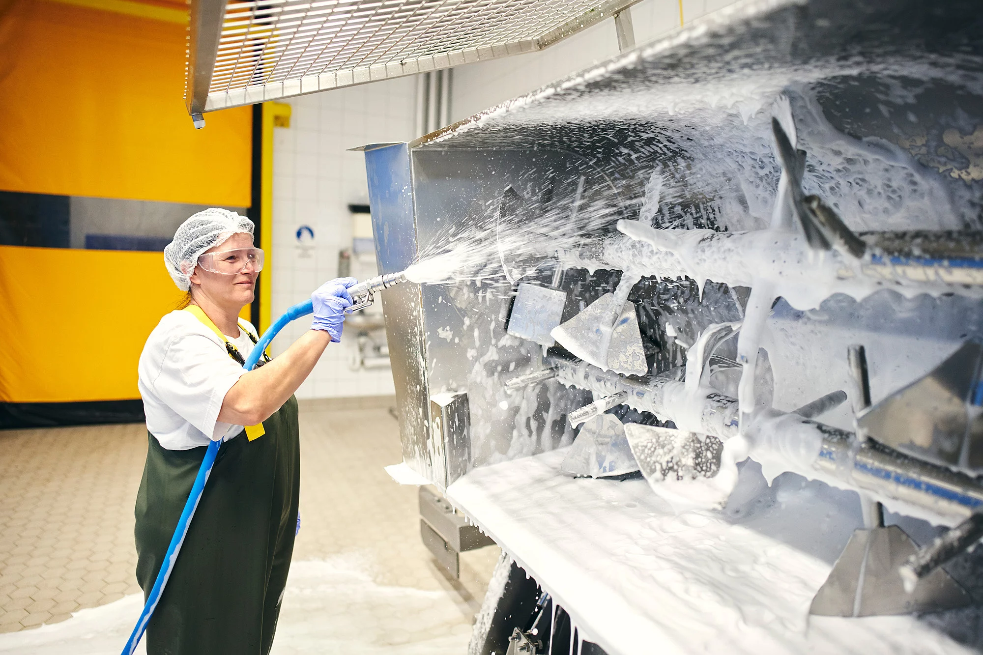 Mitarbeiterin mit einem Schlauch in der Hand, gerichtet auf die zu reinigende Maschine in der Produktion.