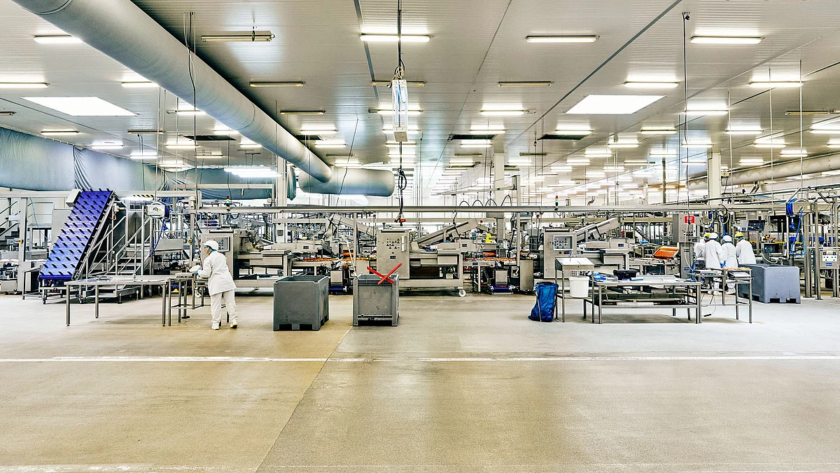 Produktionshalle mit Produktionsmaschinen an denen Mitarbeitende arbeiten. 