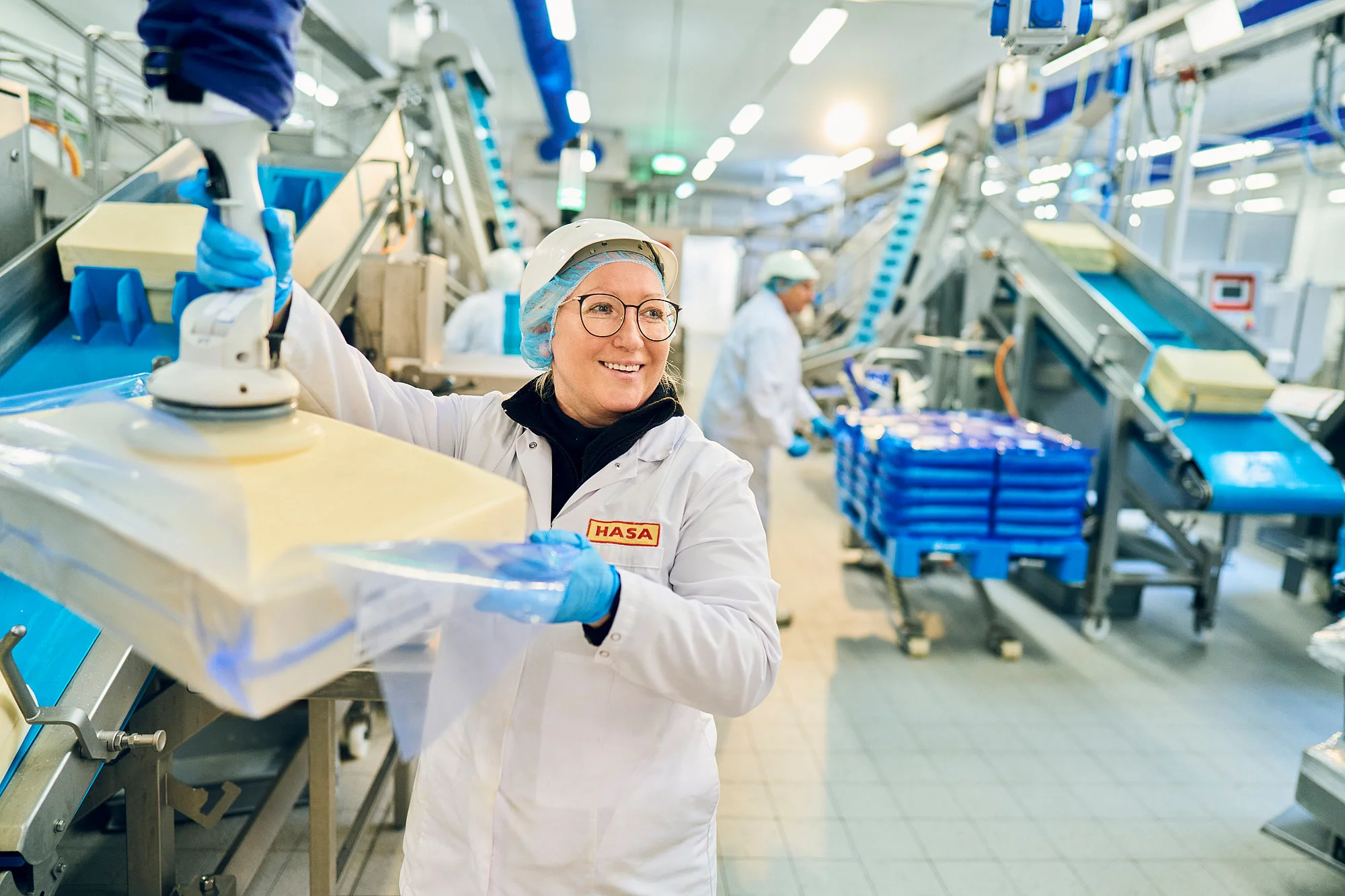 Mitarbeiterin in Arbeitskleidung in der Produktion hält Maschine in der Hand.