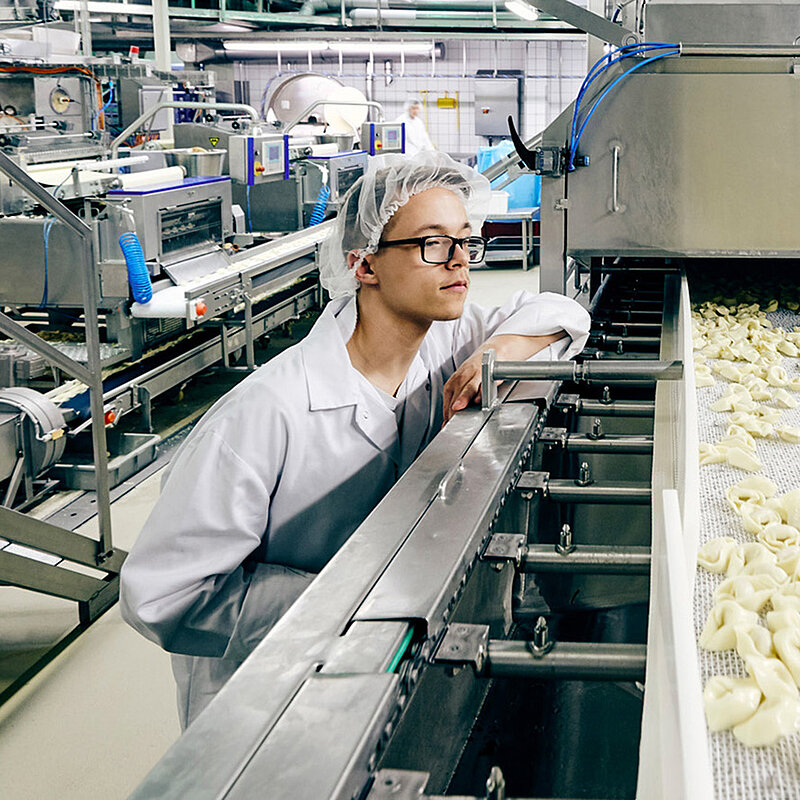 Mitarbeiter in Arbeitskleidung in Maschine reinschauend.