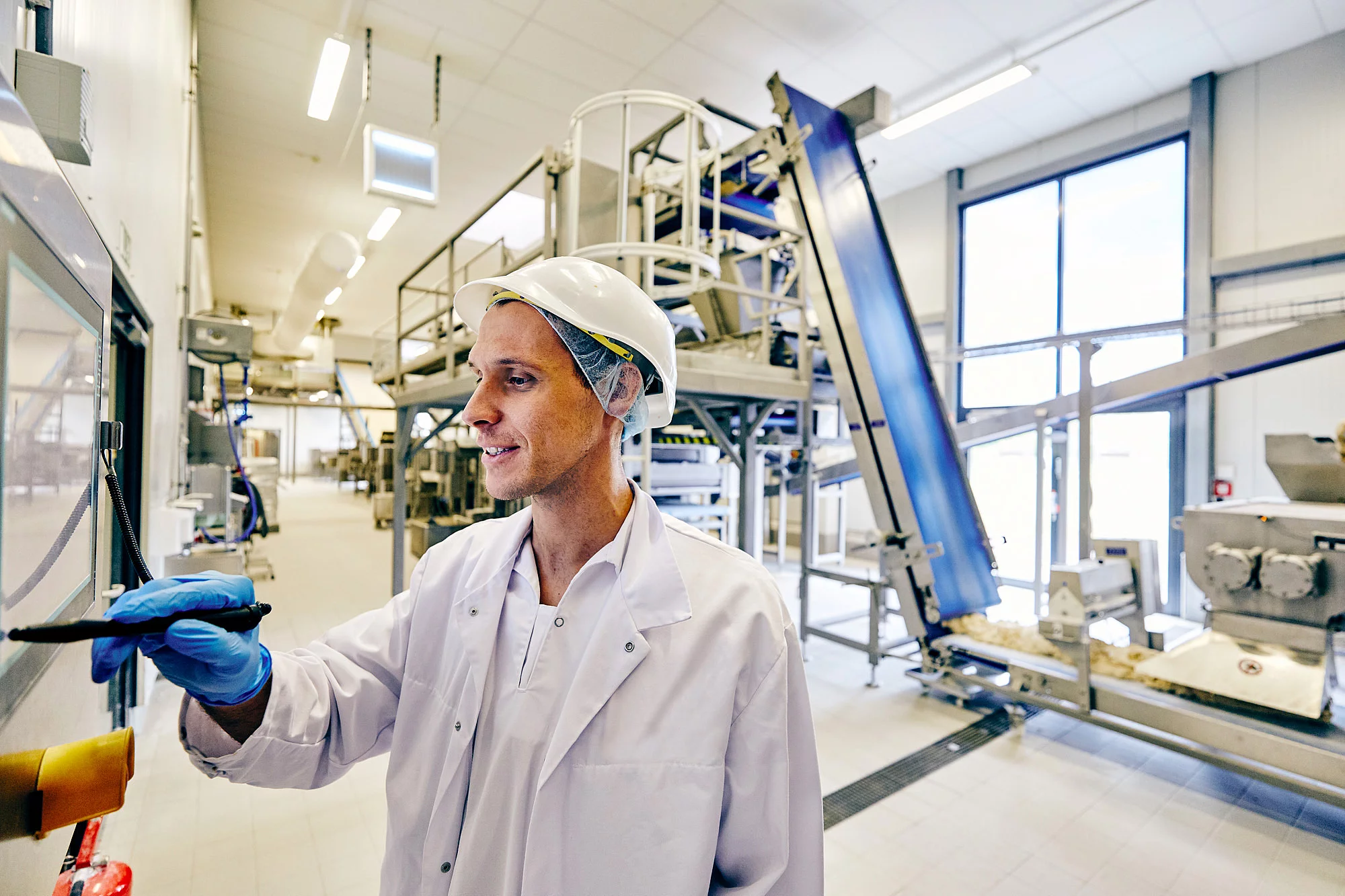 Mitarbeiter in Arbeitskleidung hält einen Stift in der Hand und schaut auf einen Bildschirm in der Produktion.