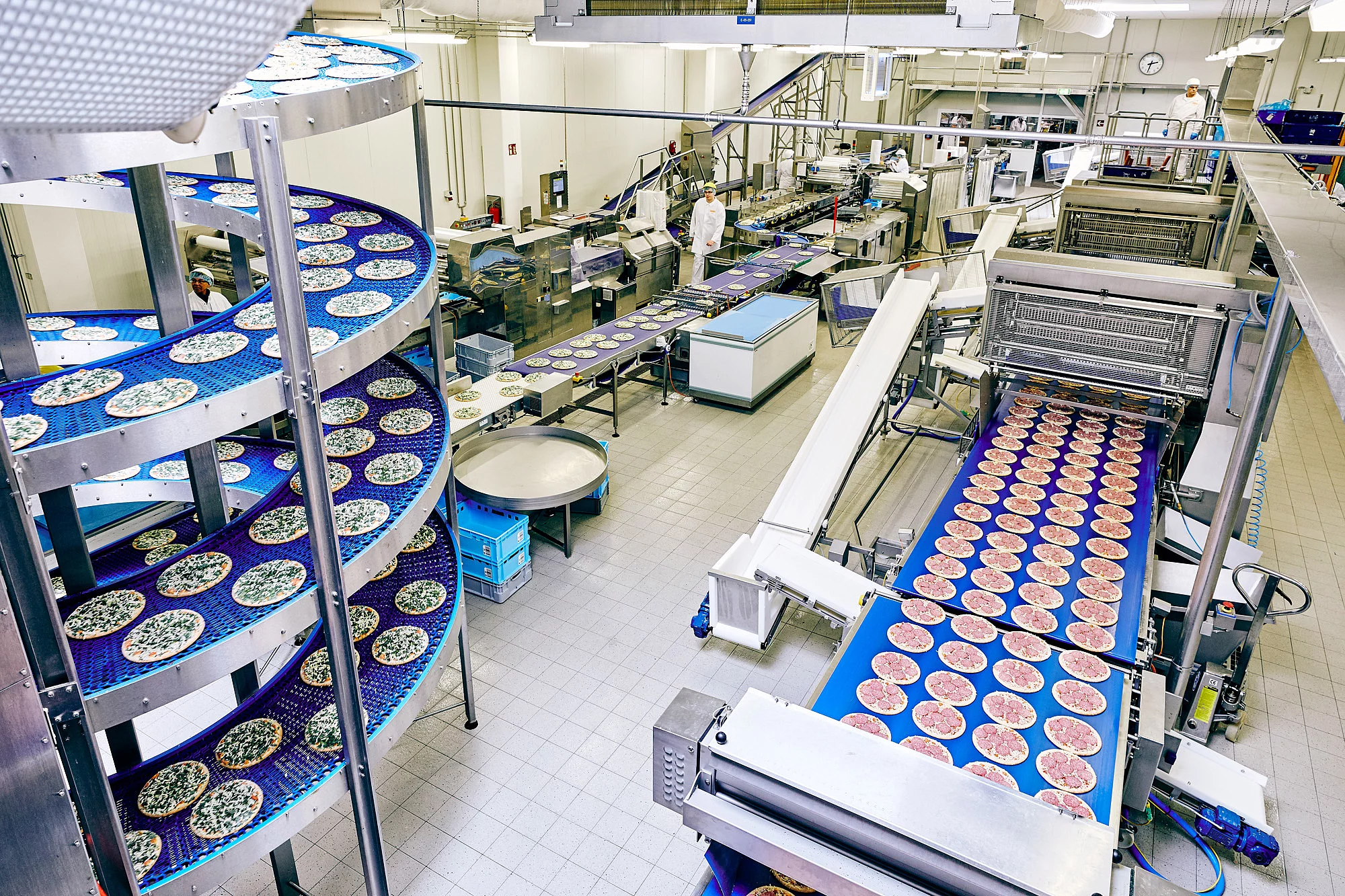 Fließbänder in einer Produktion mit Salami und Spinat Pizzen.