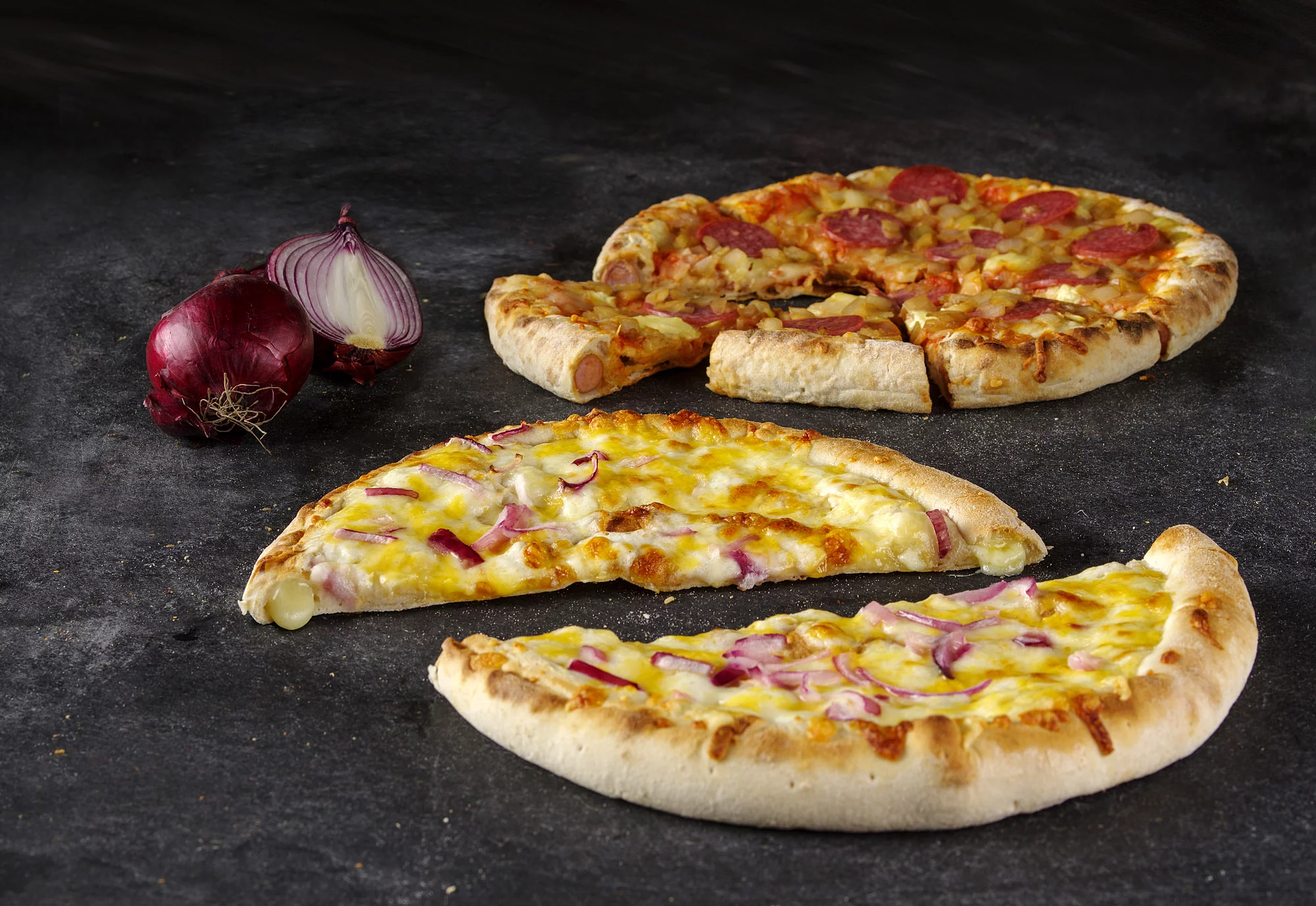 Zwei Pizzen auf einer Arbeitsplatte, angeschnitten mit einer Zwiebel drumherum dekoriert.