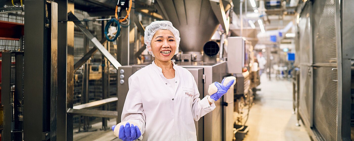 Eine Mitarbeiterin stehend in der Produktion in Arbeitskleidung.