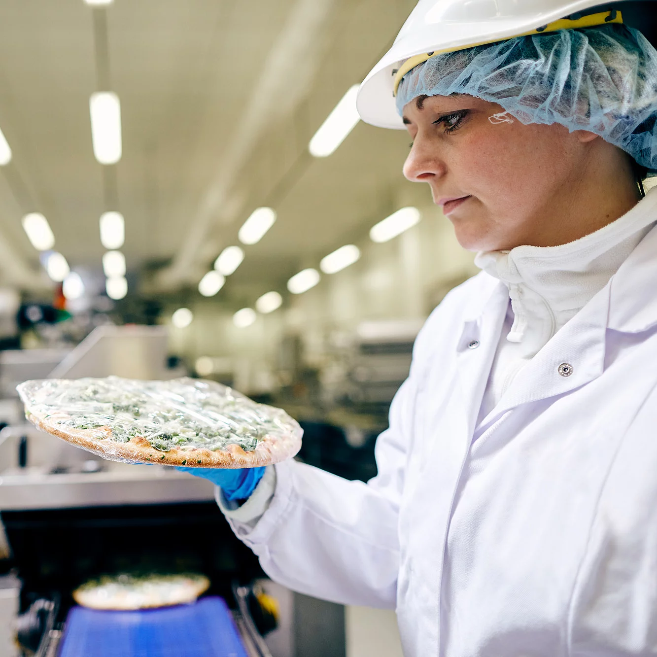 Eine Mitarbeiterin in Arbeitskleidung hält eine eingepackte Pizza in der Hand.