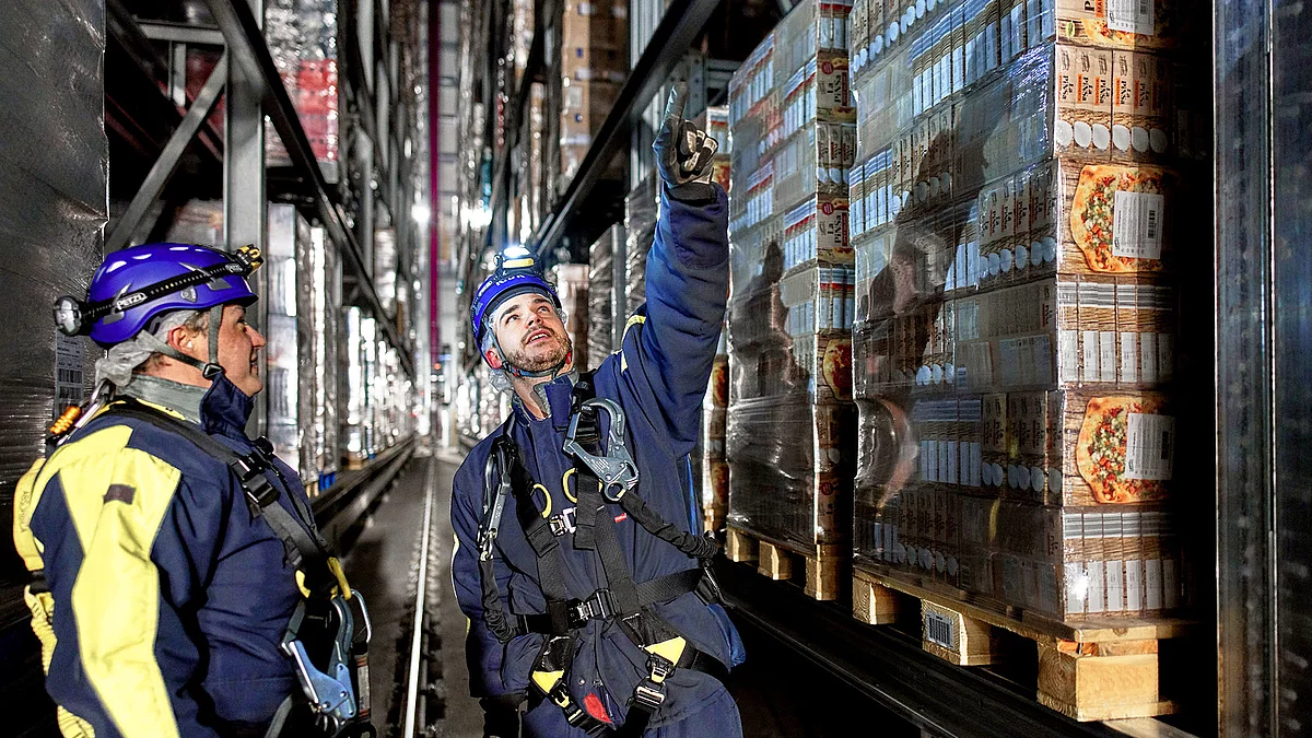 Zwei Mitarbeitende in Arbeitskleidung im Hochregallager.
