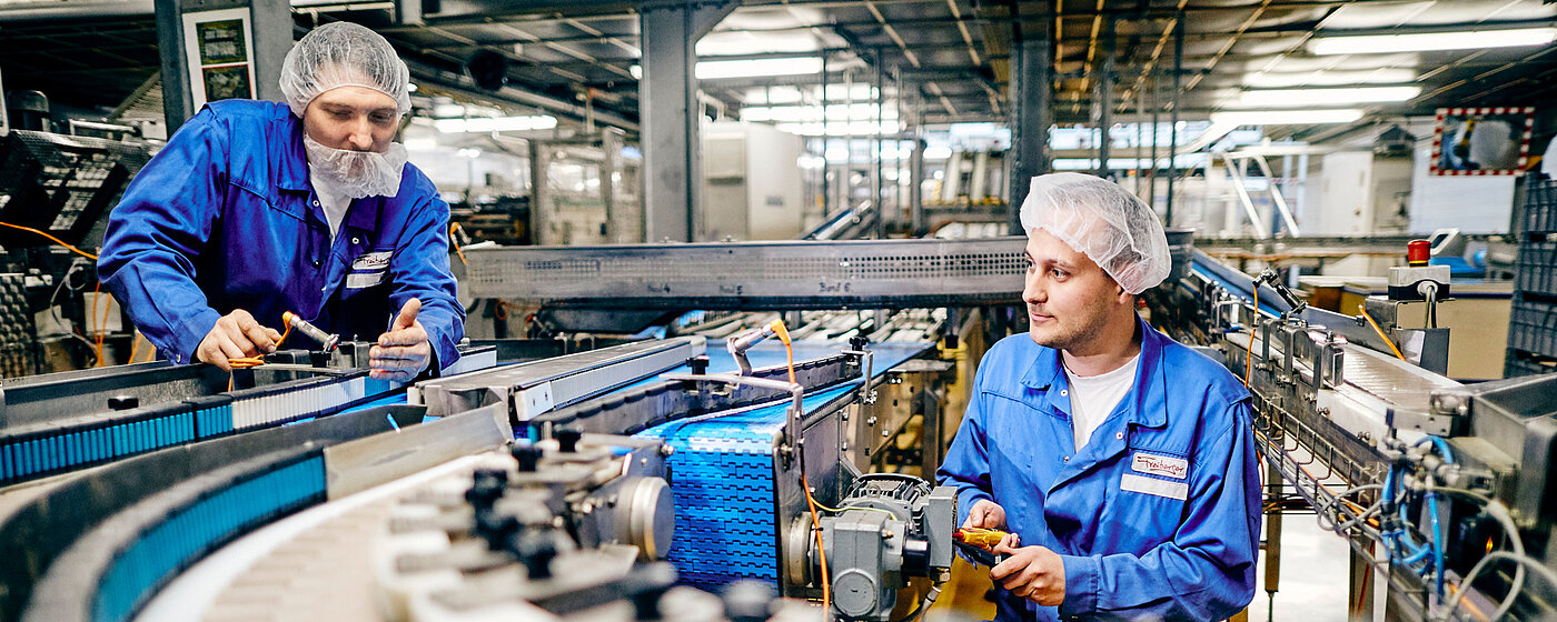 Zwei Mitarbeitende in Arbeitskleidung an der Elektronik einer Maschine.