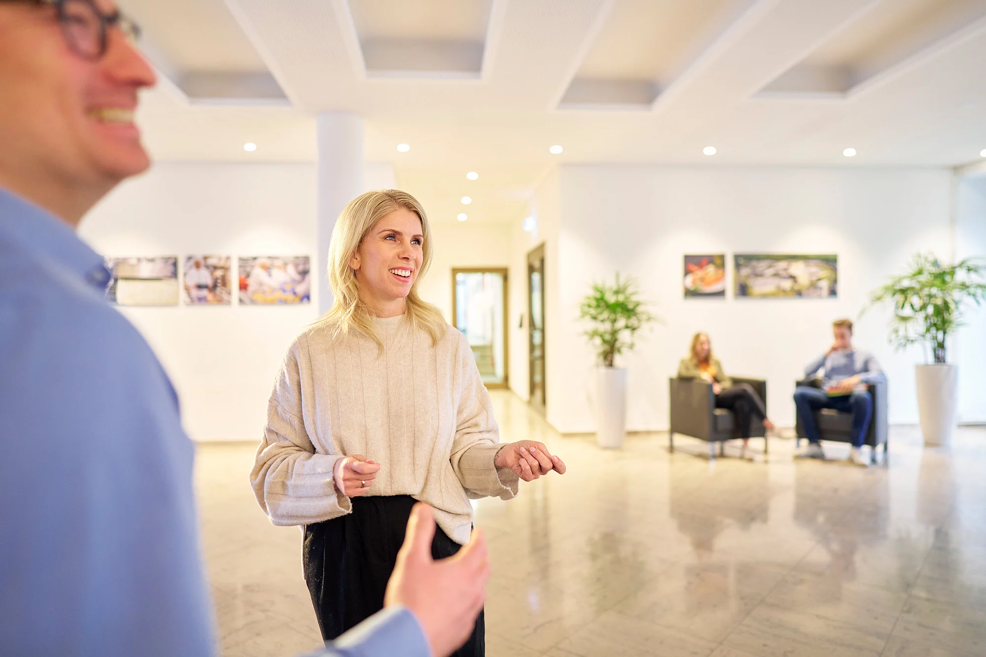 Mitarbeitende in einer Lobby am Sprechen, eine Frau lächelnd im Fokus.