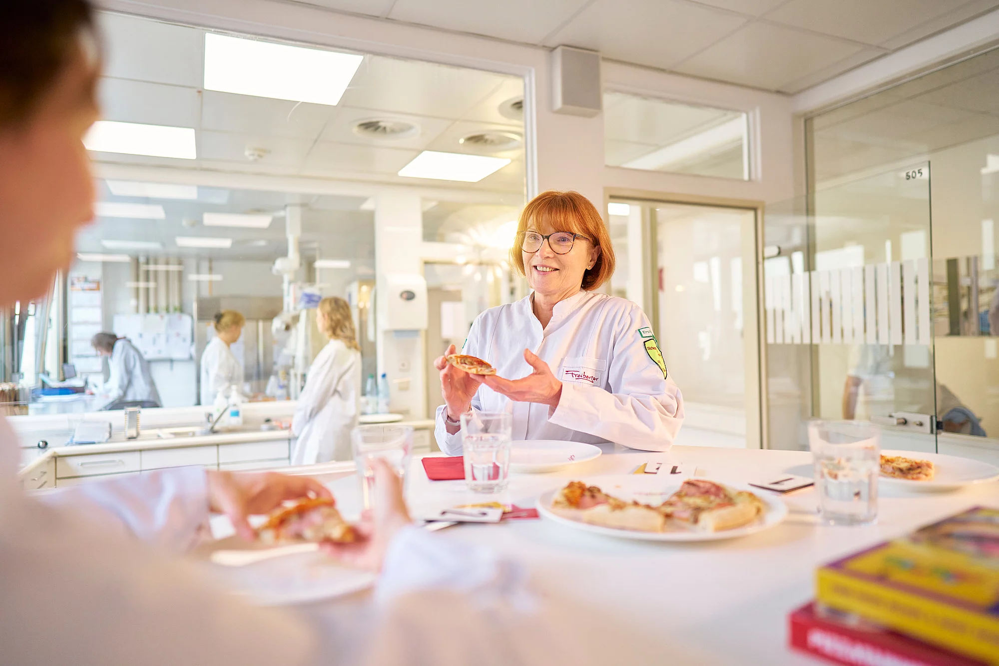 Mitarbeitende an einem Tisch mit einem Stück Pizza in der Hand.