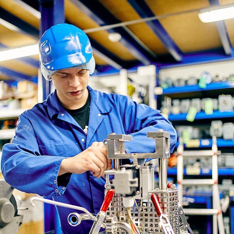 Ein Mitarbeiter in Arbeitskleidung schraubt an einer Maschine herum.
