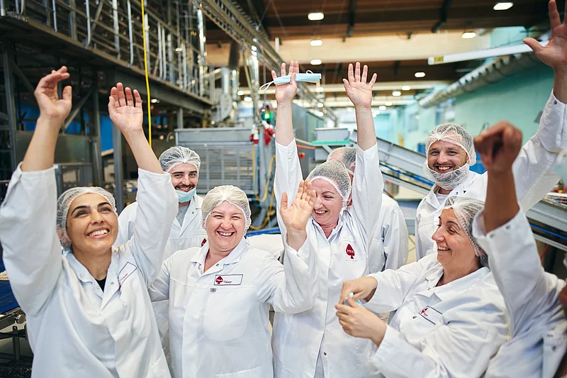 Acht Mitarbeitende stehen in Arbeitskleidung in der Produktion und sind am jubeln.