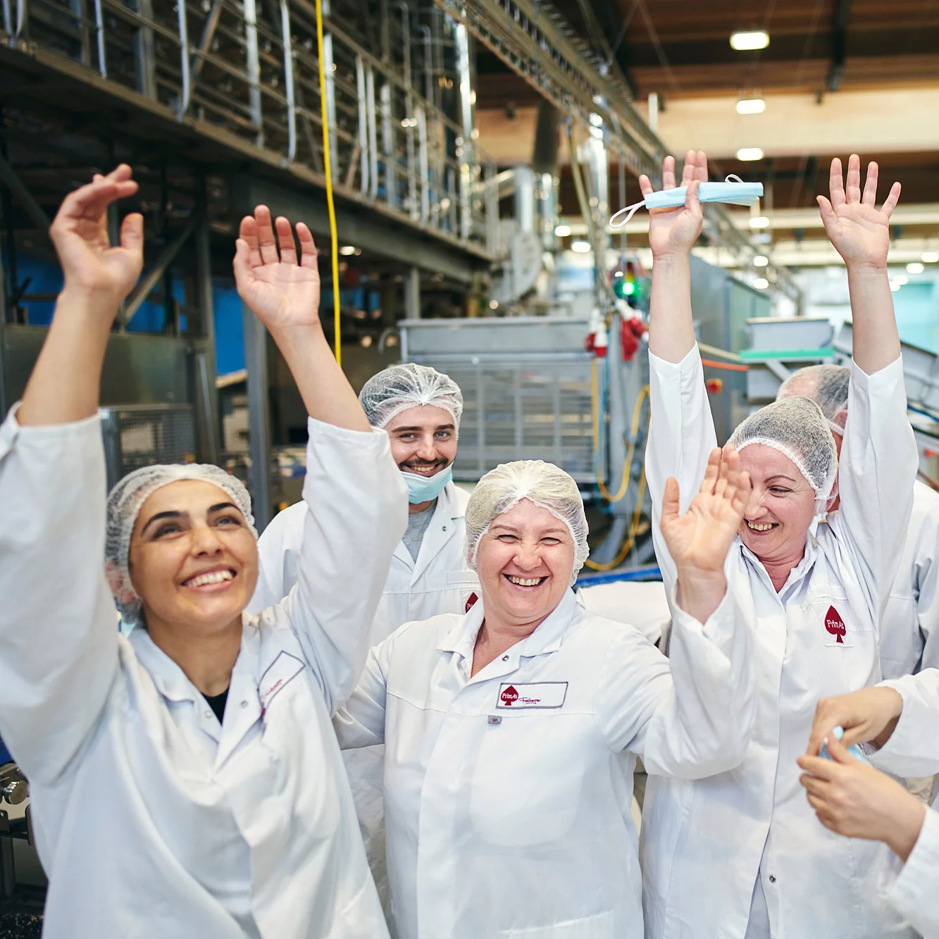 Acht Mitarbeitende stehen in Arbeitskleidung in der Produktion und sind am jubeln.
