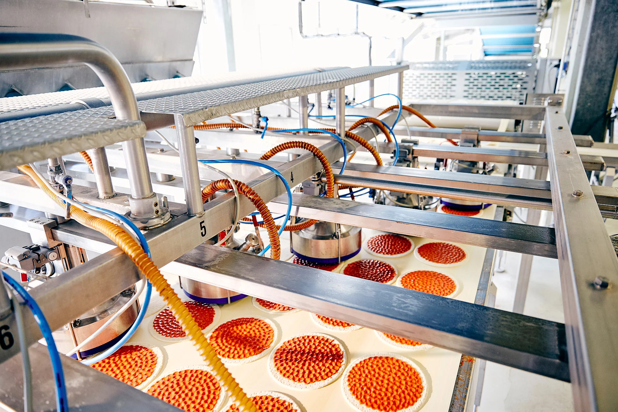 Produktionsmaschine mit Tomatensoße Schläuchen und ein Band mit Pizzaböden.