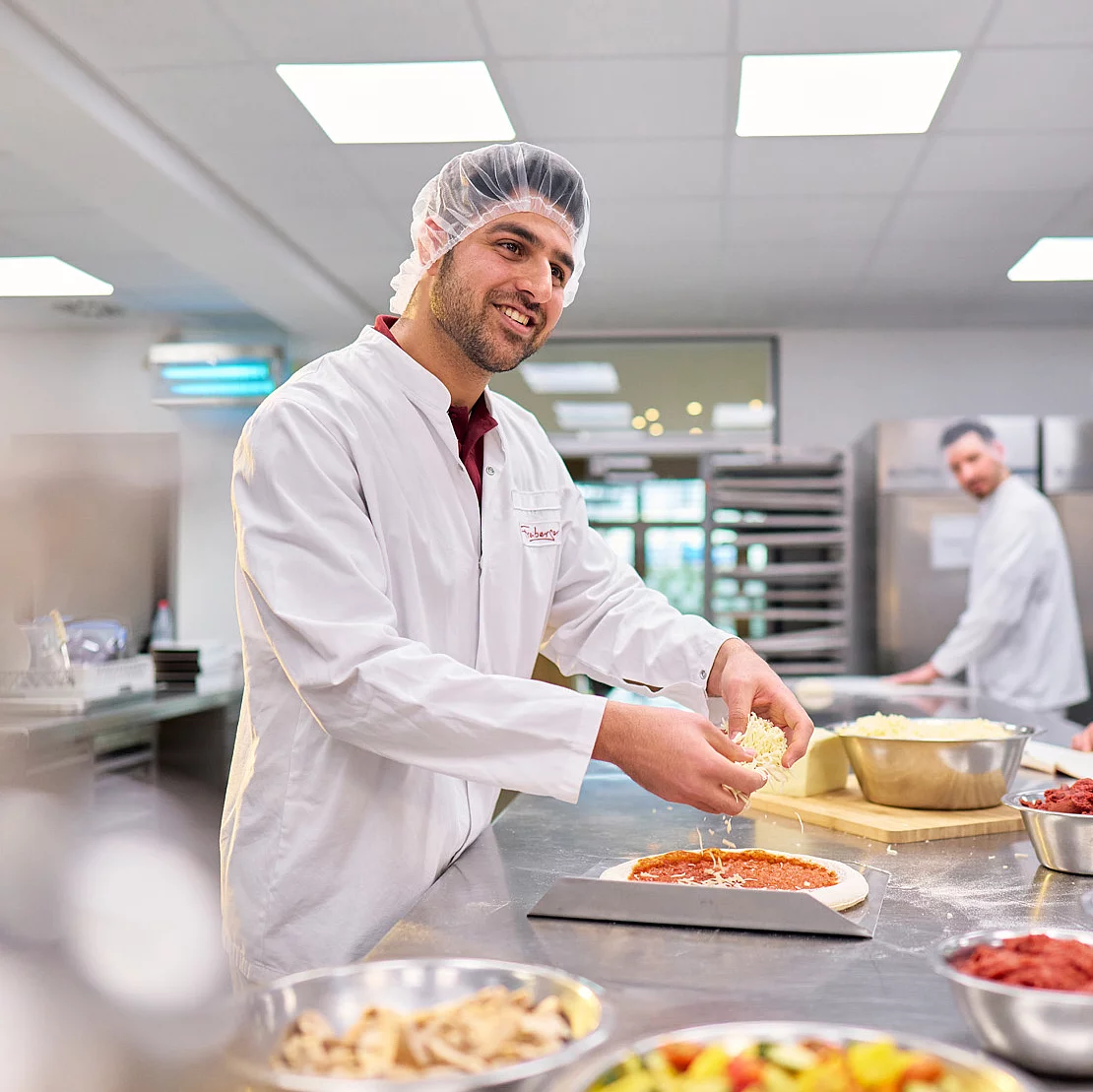 Drei Mitarbeitende in der Produktionsküche kochend am Tresen. 