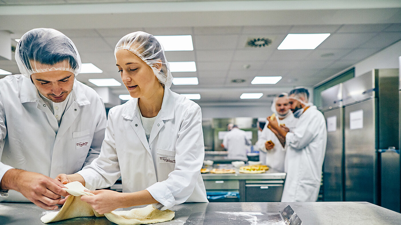 Mitarbeitende in der Küche am Ausrollen des Pizzateigs.