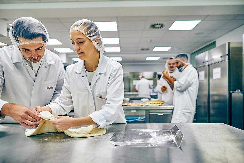 Mitarbeitende in der Küche am Ausrollen des Pizzateigs.