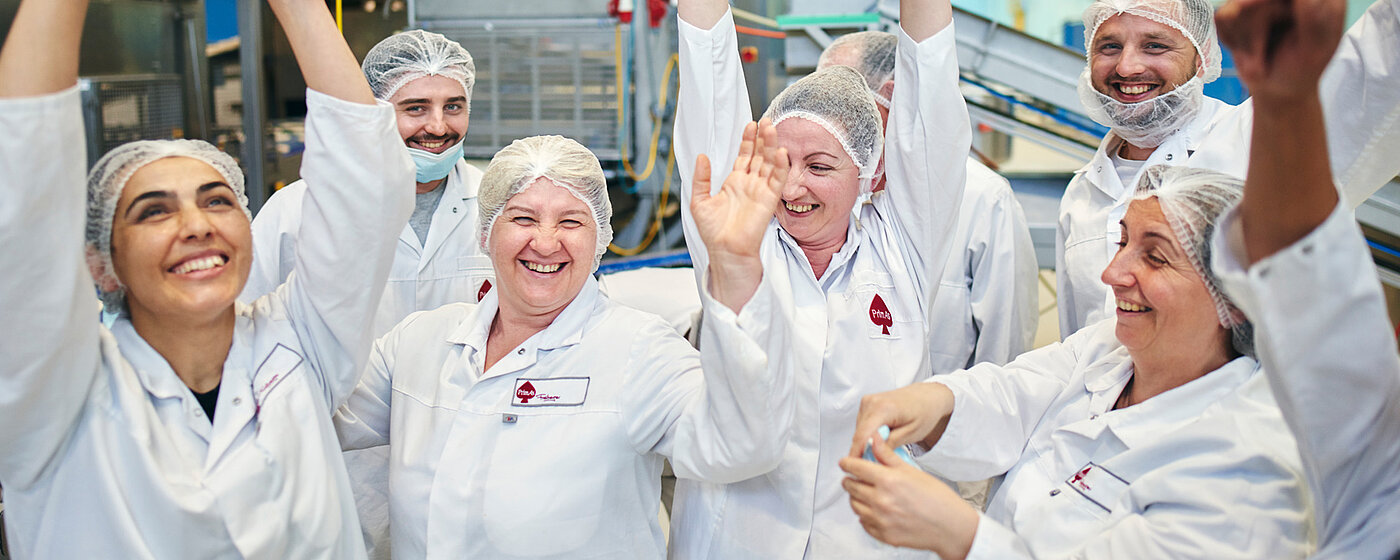 Acht Mitarbeitende jubelnd mit Armen in der Luft in der Produktionshalle.