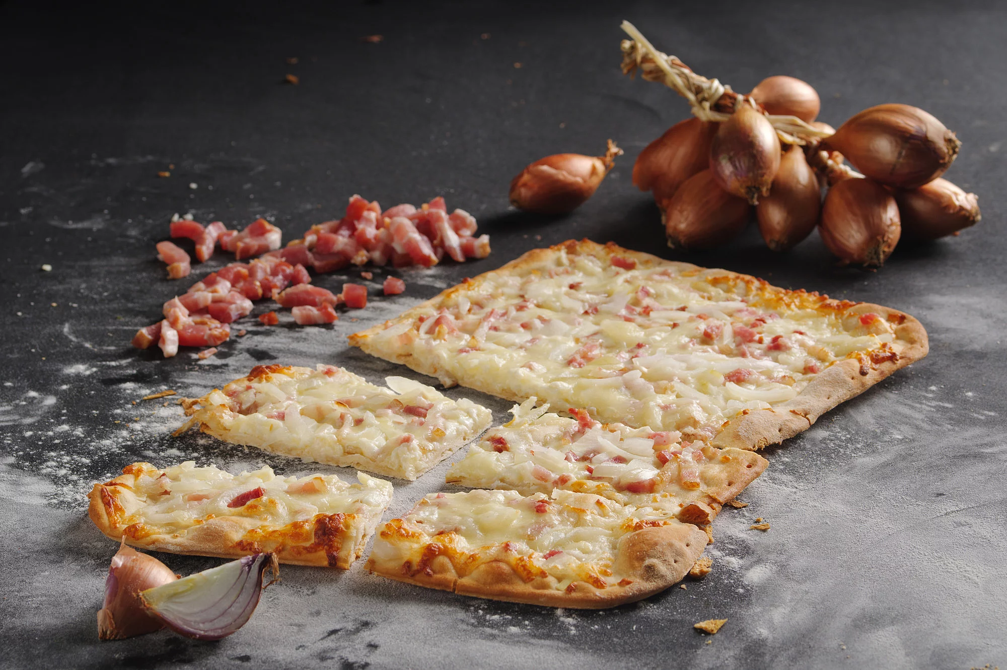 Pizzablech auf Arbeitsplatte drumherum dekoriert mit Zwiebeln und Speck.