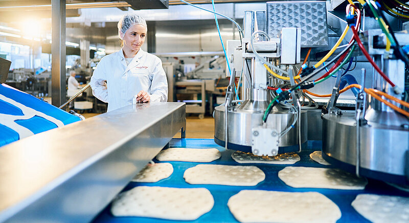 Mitarbeiterin in Arbeitskleidung an Produktionsmaschine ind er Produktion.