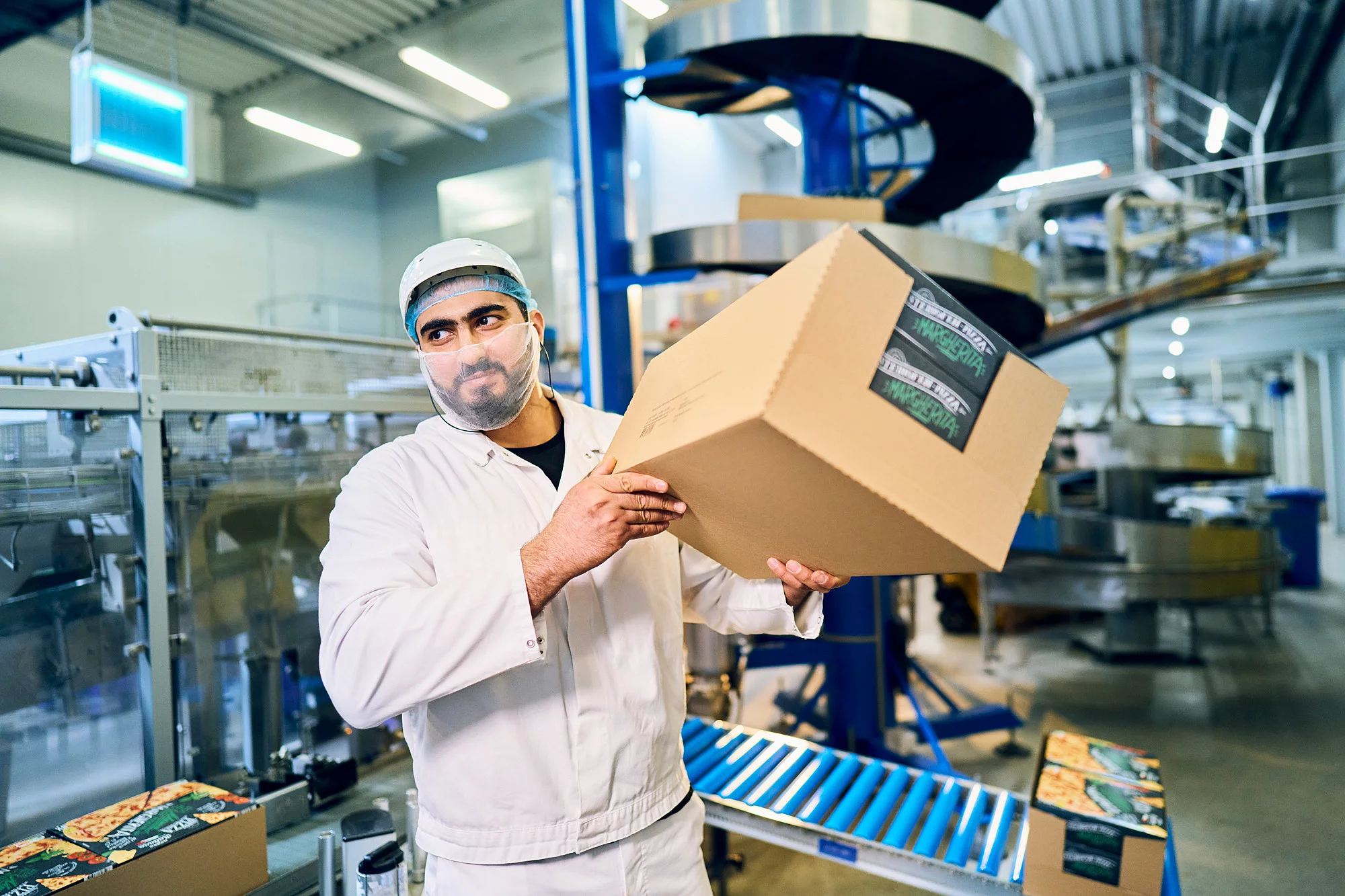Mitarbeiter in Arbeitskleidung in der Produktion hält einen großen Karton in der Hand.