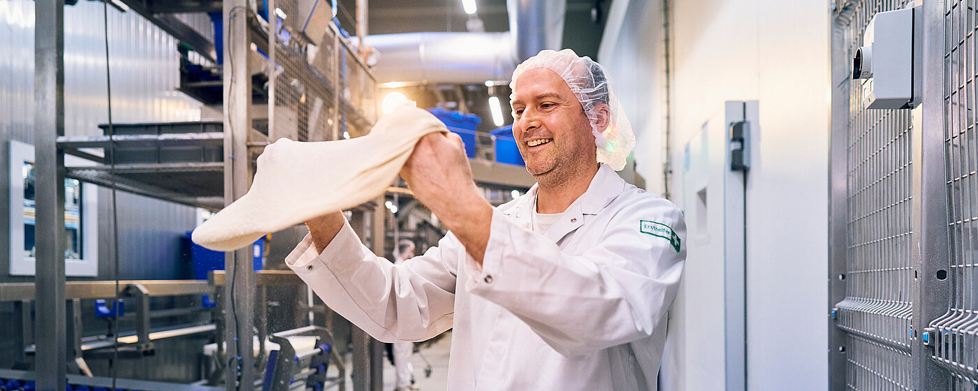 Mitarbeiter in Arbeitskleidung mit Pizzateig in der Hand.