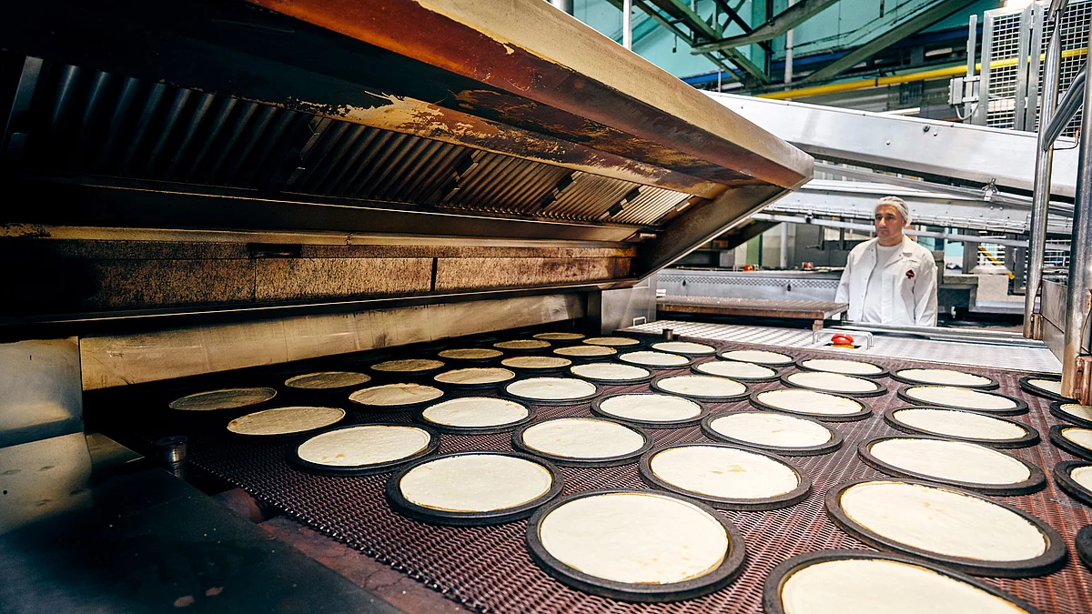 Mitarbeiter in Arbeitskleidung an Pizza-Produktions-Maschine.