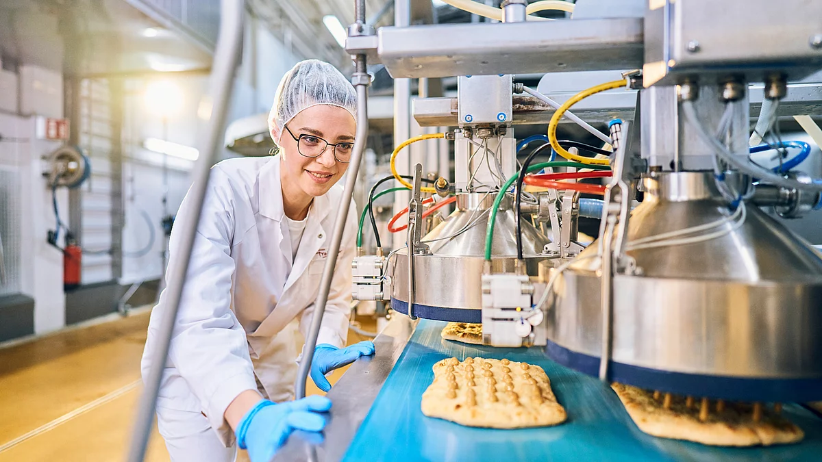 Mitarbeiterin in Arbeitskleidung an Produktionsmaschine.