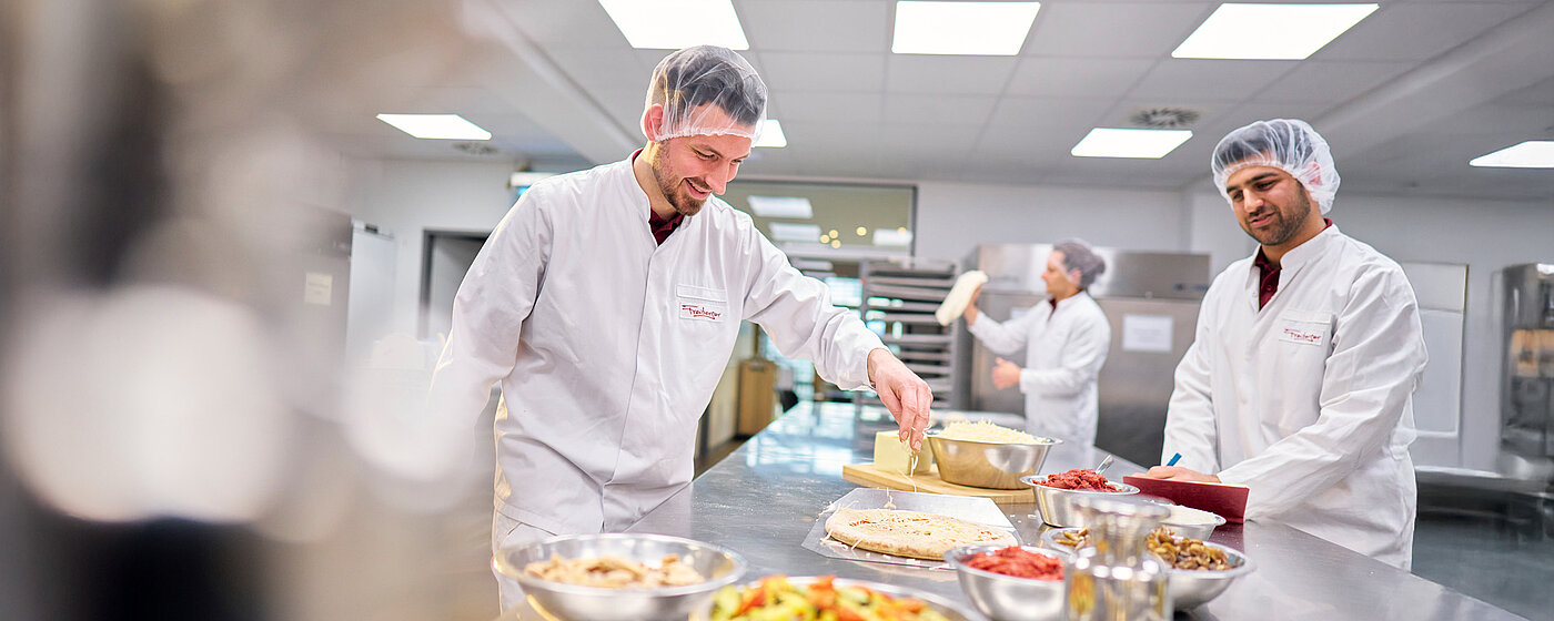 Drei Mitarbeiter in Arbeitskleidung in der Küche mit unterschiedlichen Produkten.