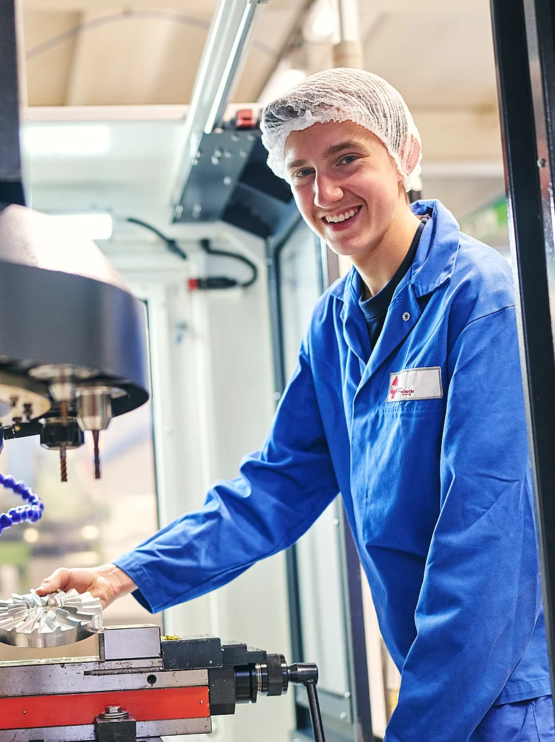 Ein Mitarbeiter steht in Arbeitskleidung an einer Maschine.