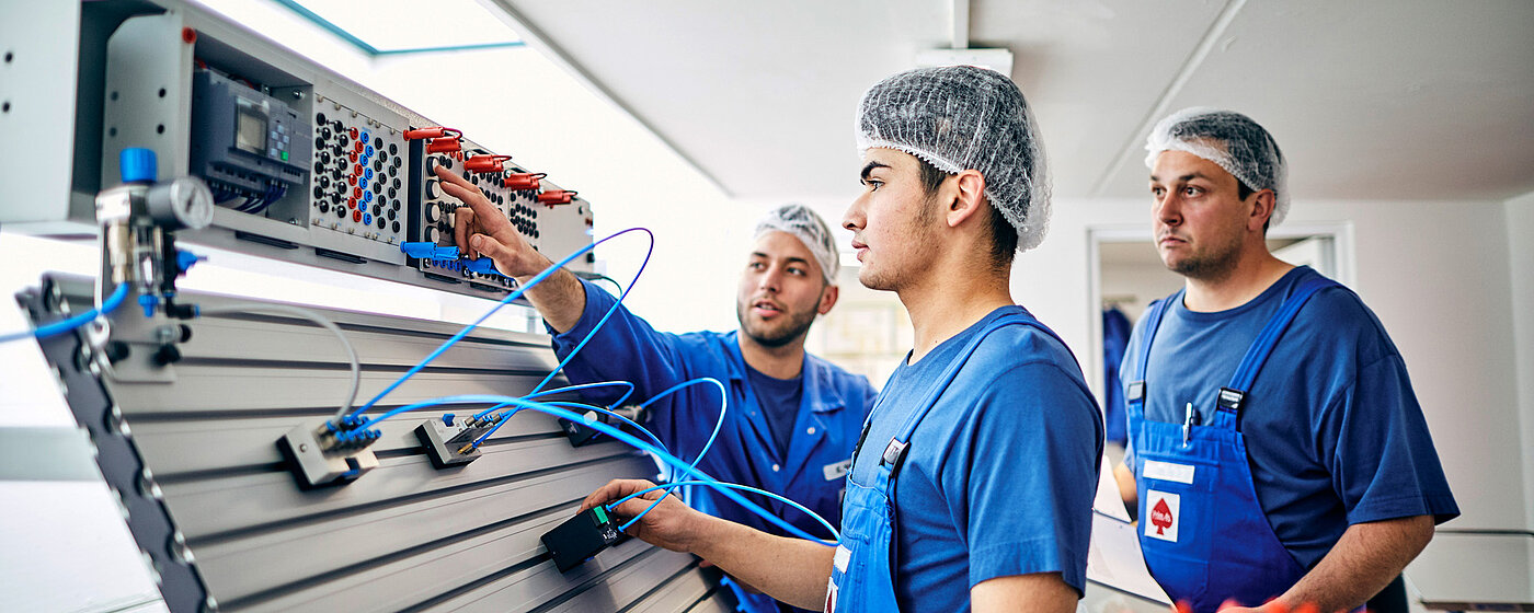 Drei Mitarbeitende in Arbeitskleidung an der Elektronik.