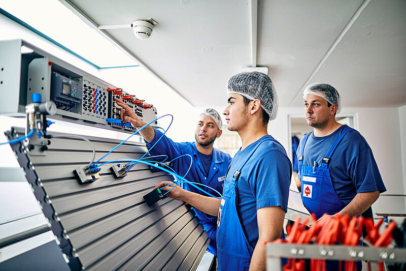 Drei Mitarbeitende in Arbeitskleidung an der Elektronik.