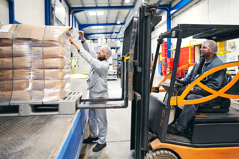 Zwei Mitarbeitende in der Produktion, am verladen der Ware mit einem Gabelstapler.