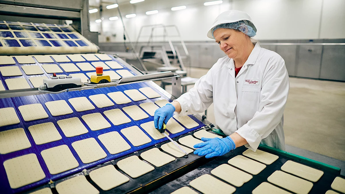 Mitarbeiterin in Arbeitskleidung steht lächelnd am Produktionsband.