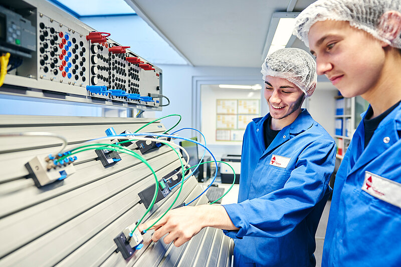 Zwei Mitarbeiter in Arbeitskleidung an der Elektronik.