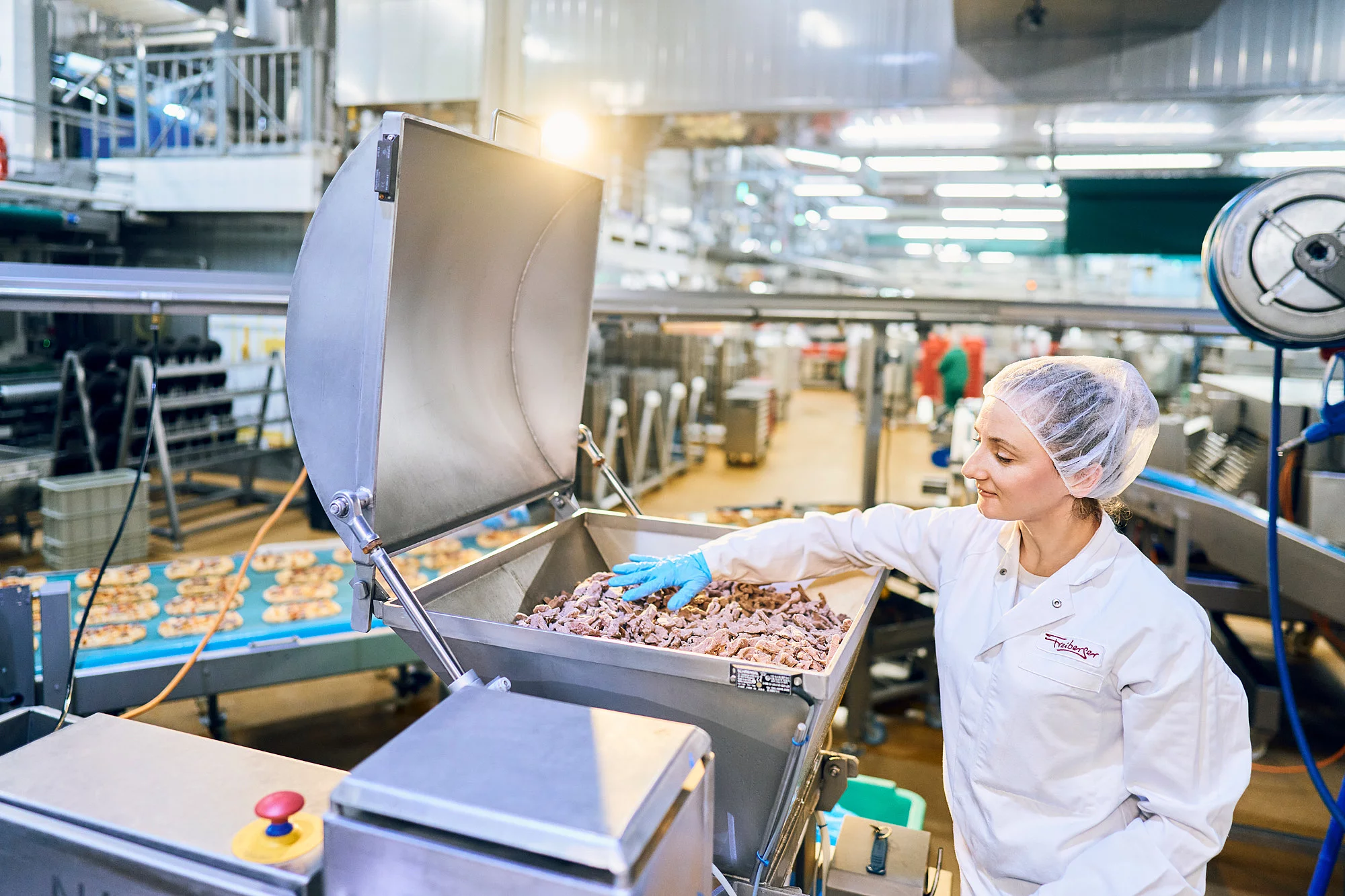 Mitarbeiterin in Arbeitskleidung in der Produktion befüllt eine Maschine mit Lebensmitteln.