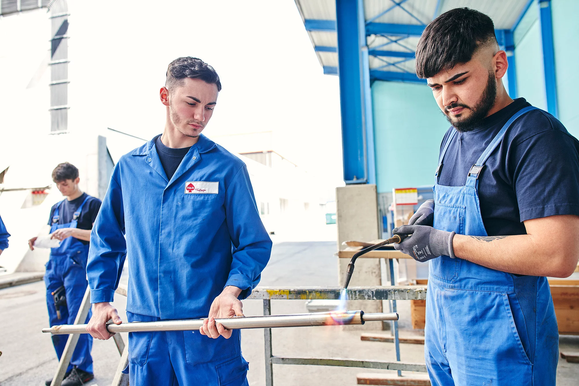Zwei Mitarbeiter stehen draußen, einer mit einer Eisenstange in der Hand und der andere mit einem Brenner.