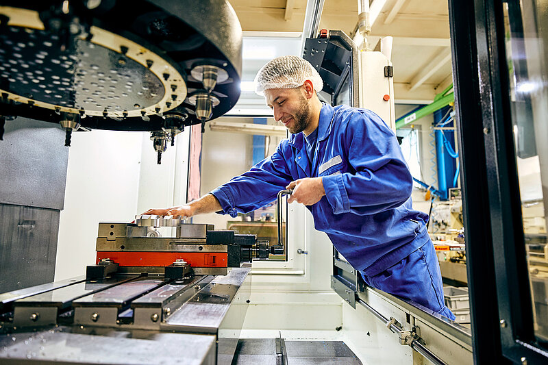 Mitarbeiter in Arbeitskleidung an einer Maschine.