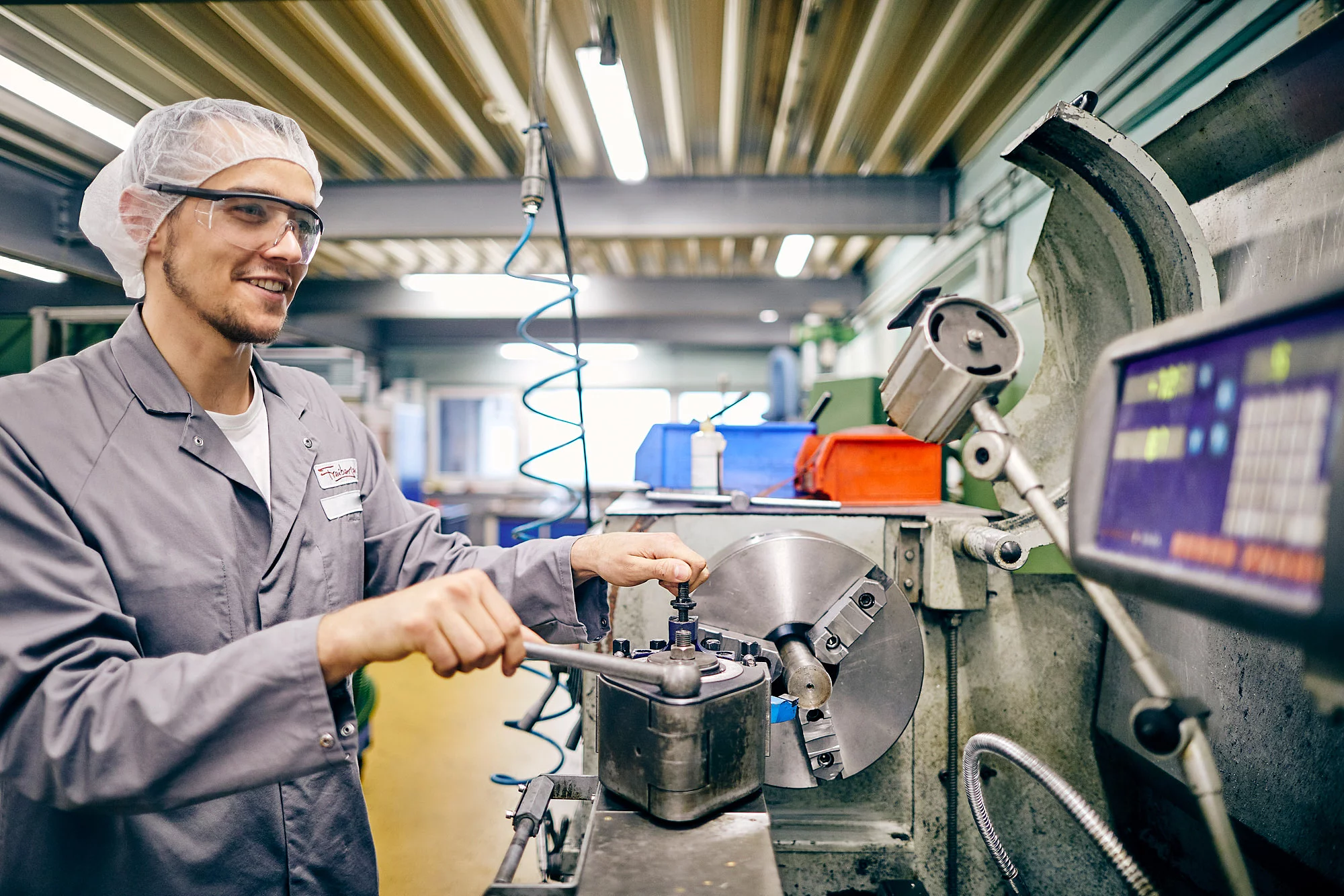 Ein Mitarbeiter steht in Arbeitskleidung vor einer Maschine und hält Werkzeug in der Hand.