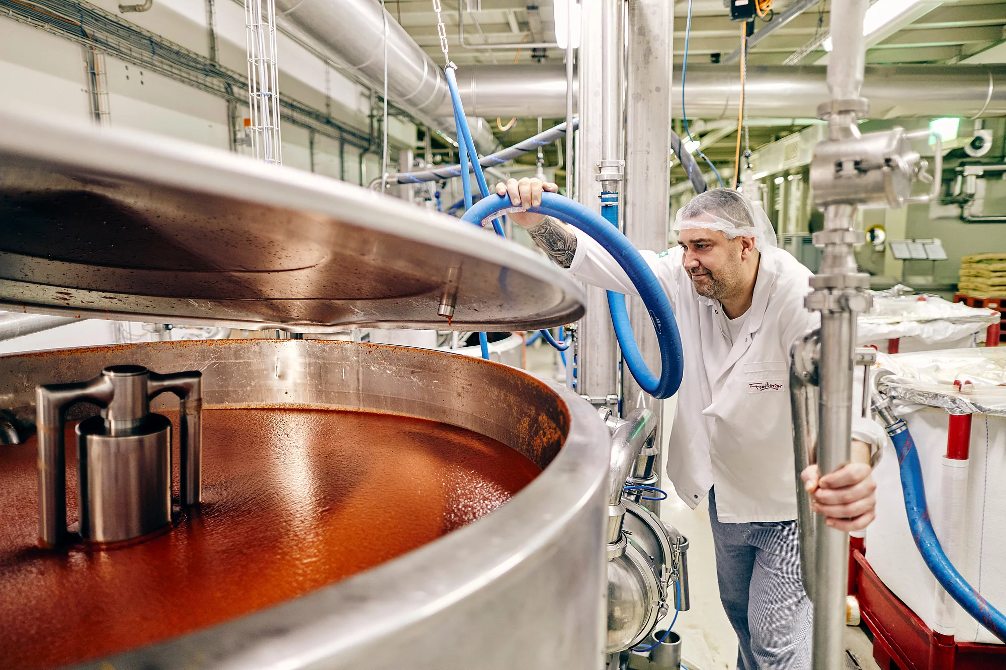 Mitarbeiter in Arbeitskleidung in der Produktion vor einer Maschine voller Tomatensoße.