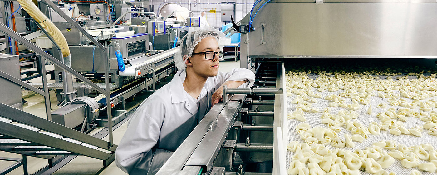 Mitarbeiter in Arbeitskleidung in eine Maschine reinschauend.