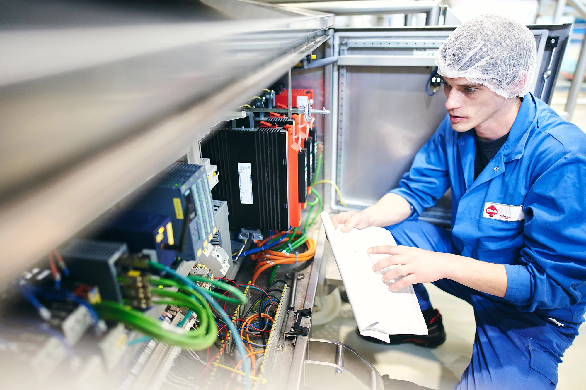 Mitarbeiter in Arbeitskleidung vor einer Maschine mit einem Blatt Papier in der Hand.